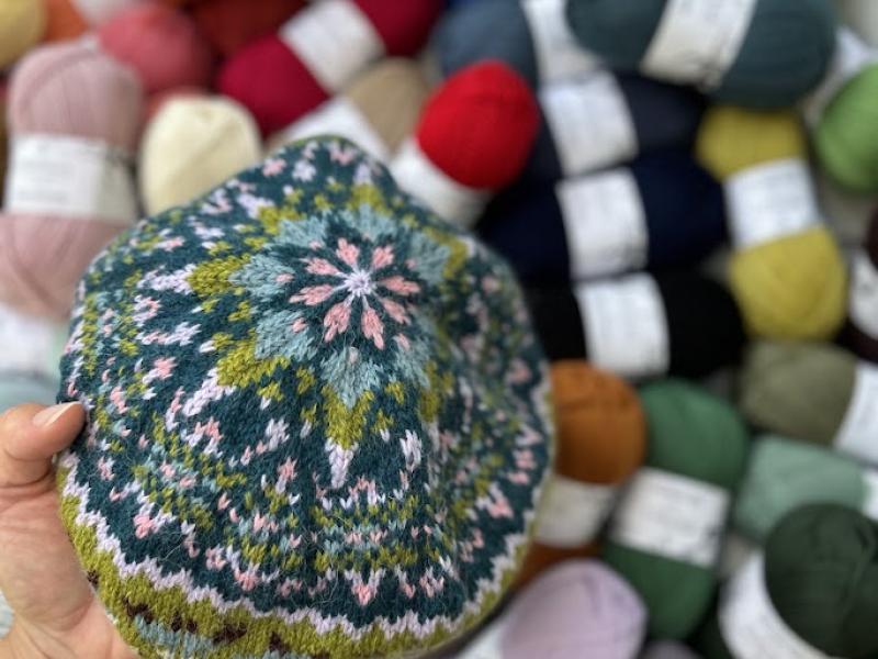 Billedet forestiller en hue strikket i fair isle med en masse garnnøgler i baggrunden.